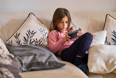 Young woman using mobile phone while sitting on sofa at home