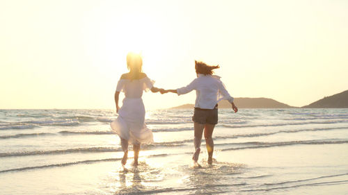 Rear view of two women walking on beach against sky