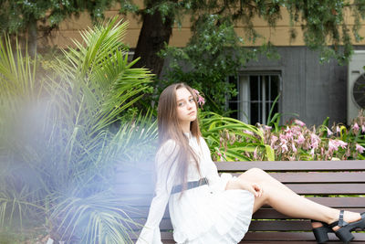 Young woman sitting on bench against plants