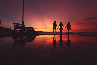 Silhouette women on beach against sky at sunset