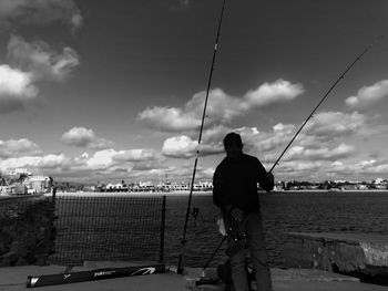 Rear view of man fishing in sea against sky