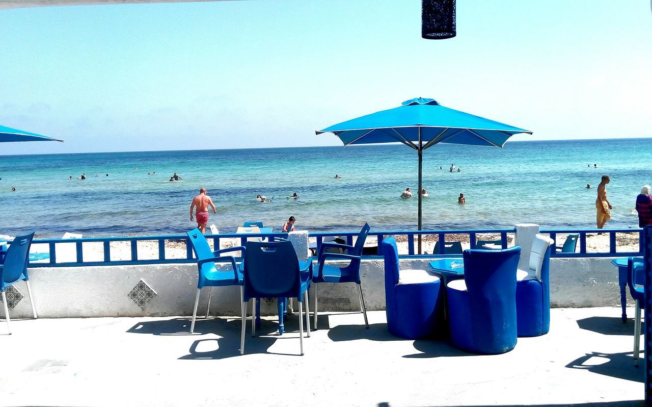 horizon over water, sea, chair, beach, water, table, relaxation, clear sky, tranquility, leisure activity, tranquil scene, empty, rear view, beach umbrella, umbrella, vacations, sunshade, blue, scenics, nature, person, day, summer, beauty in nature, arrangement, tourism