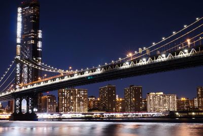 Illuminated bridge over river and buildings at night