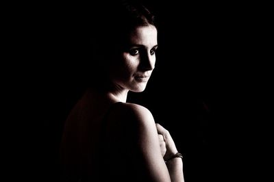 Close-up portrait of young woman against black background