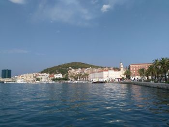 Buildings by sea against blue sky