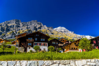 Houses amidst trees and buildings against clear blue sky