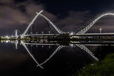 Illuminated bridge over river against sky at night