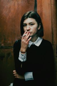 Young woman smoking against rusty wall