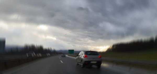 Cars on road against cloudy sky