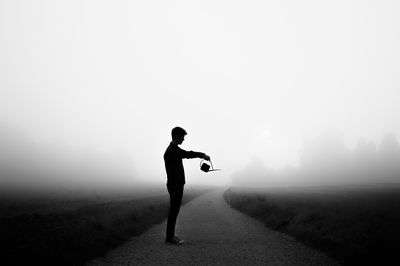 Silhouette man standing on mountain in foggy weather