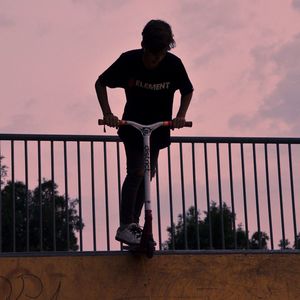 Man standing by railing against sky during sunset