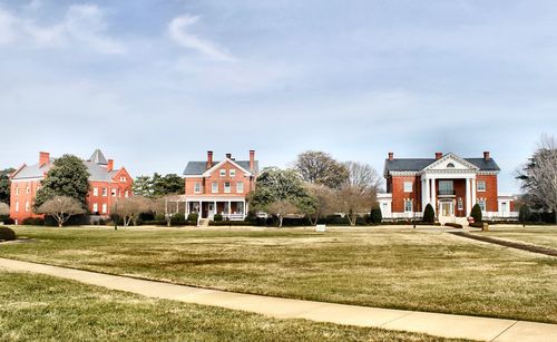 Scenic view of buildings next to park against cloudy sky