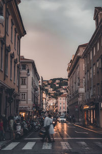 People walking on city street amidst buildings against sky