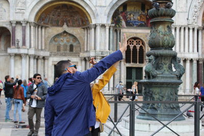 People gesturing stop sign while standing against statue in city