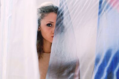 Portrait of beautiful woman hiding behind curtains