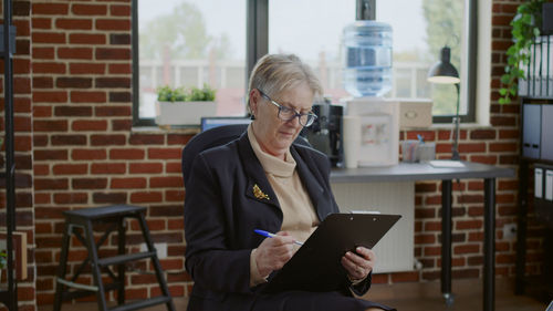 Senior woman writing on clipboard in office