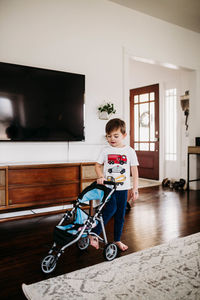 Young boy pushing stroller with stuffed animal in livingroom