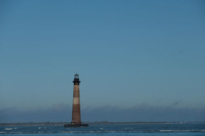 Lighthouse by sea against clear sky