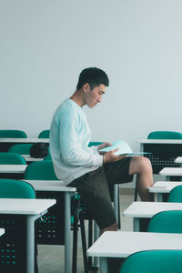 Side view of young man sitting with book on table in classroom