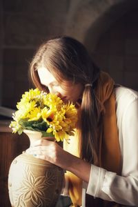 Close-up of young woman smelling yellow flowers in vase
