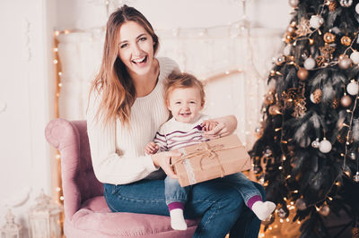 Smiling mother and daughter holding gift box at home
