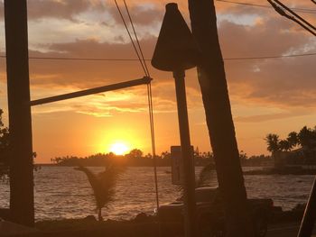 Silhouette wooden post by sea against sky during sunset