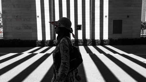 Side view of young woman walking on footpath during sunny day