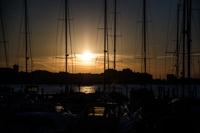 Sailboats moored at harbor against sky during sunset
