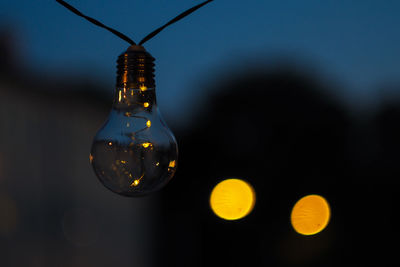 Close-up of light bulb hanging outdoors at dusk