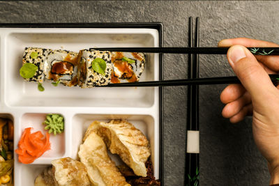 Cropped image of hand holding sushi with chopsticks in plate