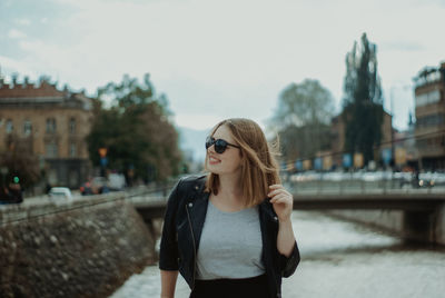 Smiling woman standing against river in city 