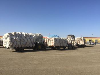 Stack of firewood by road against clear blue sky