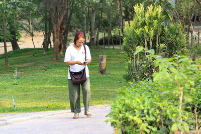 Full length of mature woman using mobile phone while standing in park