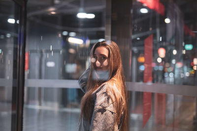 Portrait of smiling young woman standing against illuminated building