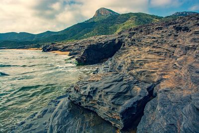 Scenic view of rocky mountains by sea against sky