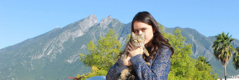 Portrait of beautiful woman carrying cat against rocky mountains