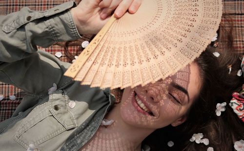 Directly above shot of smiling girl holding hand fan while lying on textile