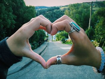 Cropped hands of people making heart shape against trees