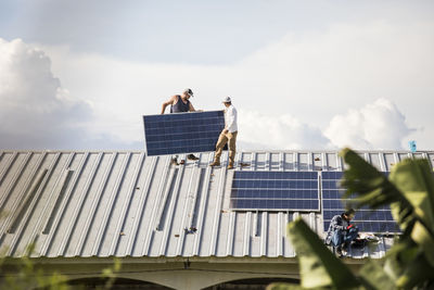 Team of electricians work to install solar panels on rooftop.