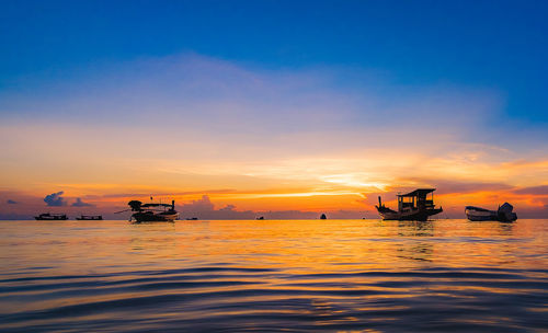 Silhouette boats in sea against sky during sunset