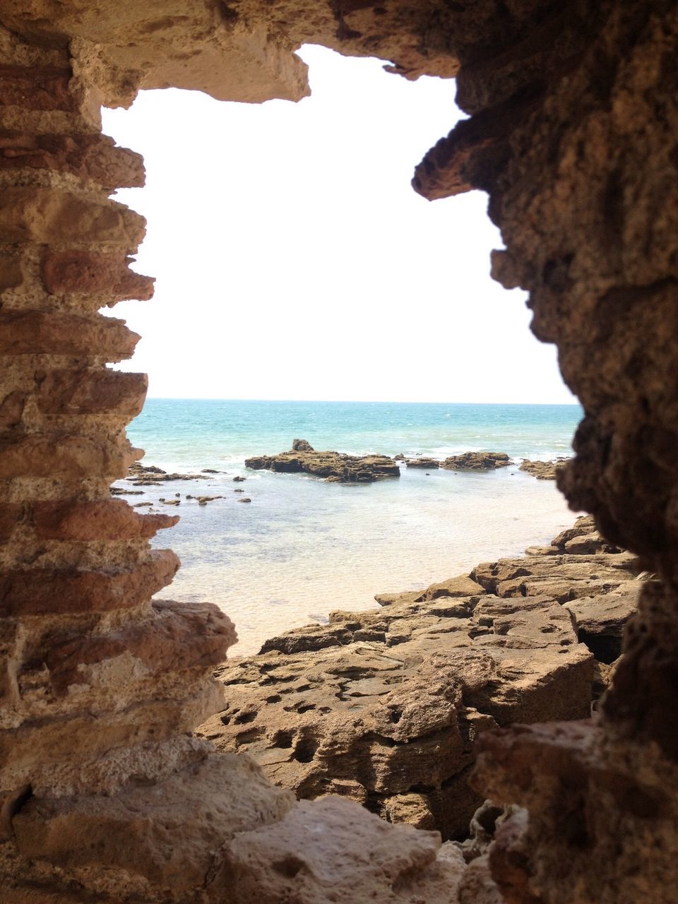 sea, horizon over water, water, clear sky, built structure, rock - object, architecture, rock formation, beach, tranquility, scenics, nature, indoors, tranquil scene, beauty in nature, shore, sky, sunlight, arch, day