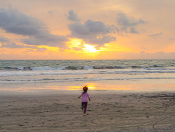Rear view on girl running at beach against cloudy sky during sunset