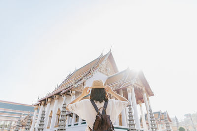 Rear view of woman standing by building against sky