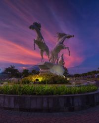 Statue by fountain against sky at sunset