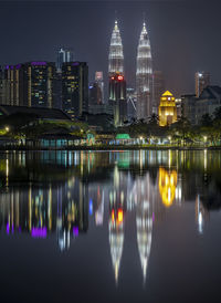 Illuminated buildings by river against sky at night