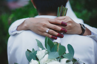 Cropped hands of bride holding bouquet while embracing bridegroom