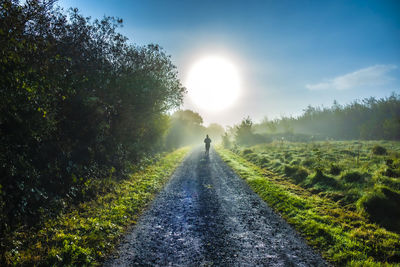 Rear view of woman running on dirt road against sky