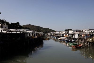Boats moored on canal by buildings against sky