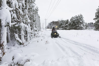 Rear view of teenage boy driving quadbike on snow covered field against sky