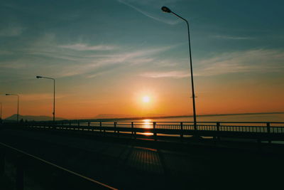 Silhouette street by sea against sky during sunset
